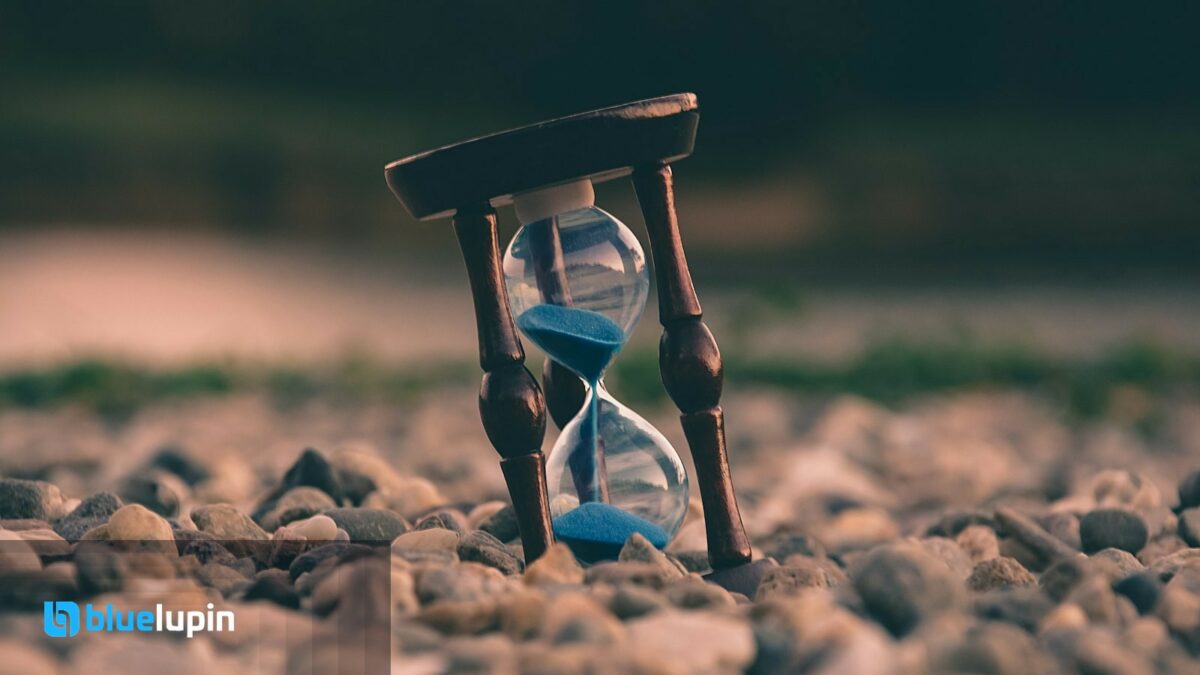Wooden hourglass with blue sand on river stones; Bluelupin lockup bottom left